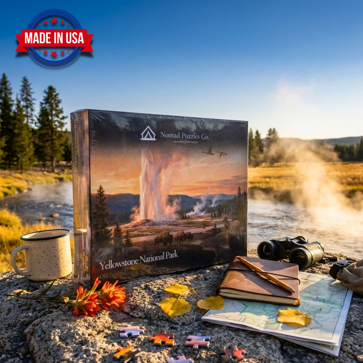 Nomad Puzzles Co. Yellowstone Old Faithful 1,000-piece puzzle box on a boulder beside the steaming Firehole River at golden hour